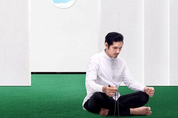 Asian Muslim man praying with prayer beads on his hands