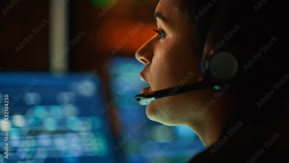 Poster Close Up Portrait of Multiethnic Female IT Technical Support Specialist Talking with a Client in Headphones and Working on Desktop Computer in Monitoring Control Room with Big Digital Screens.
