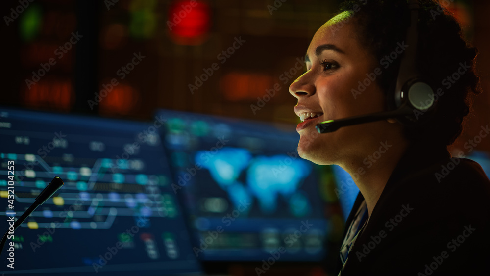 Poster Close Up Portrait of Multiethnic Female IT Technical Support Specialist Talking with a Client in Headphones and Working on Desktop Computer in Monitoring Control Room with Big Digital Screens.