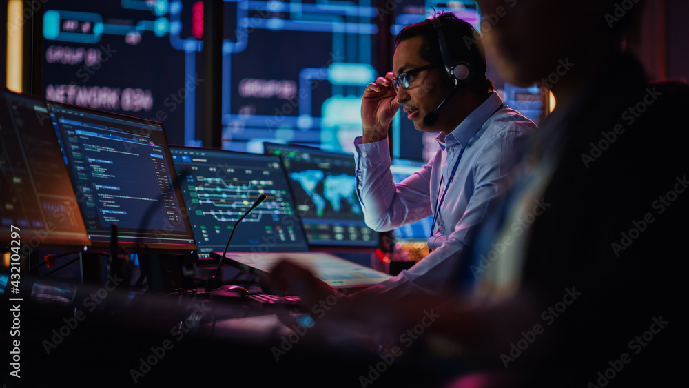 Aufkleber Professional IT Technical Support Specialist and Software Developer Working on Computer in Monitoring Control Room with Digital Screens. Employee Uses Headphones with Mic, Talking on a Call.