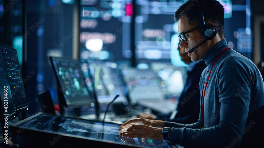 Fototapete Portrait of Professional IT Technical Support Specialist Working on Computer in Monitoring Control Room with Digital Screens. Employee Wears Headphones with Mic and Talking on a Call.