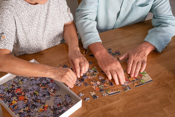 Hands of two elderly people at home  playing with jigsaw puzzle on wooden table