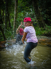 Two young girls wearing sporty clothes splashing each other water in a forest river in Malaysia.  