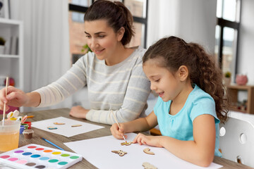 family, hobby and leisure concept - happy smiling mother spending time with her little daughter drawing or painting wooden chipboard items with colors at home