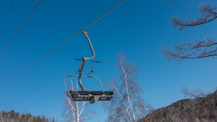 Empty seat of the chairlift against the backdrop of a bright blue sky. Bare branches of trees and...