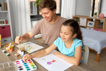 family, motherhood and leisure concept - happy smiling father spending time with his little daughter and drawing with colors at home