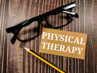 Medical concept.Text PHYSICAL THERAPY with glasses and pencil on a brown wooden background.