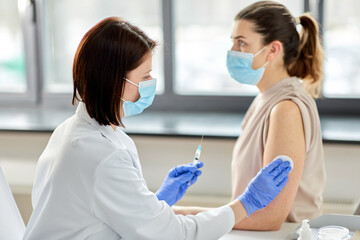 Fototapeta premium health, medicine and pandemic concept - female doctor or nurse wearing protective medical mask with syringe vaccinating patient at hospital