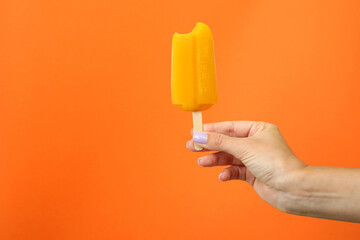 Female hand hold ice cream stick on orange background