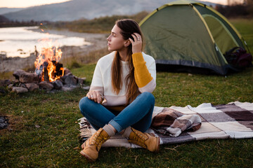 Front view of young brunette in the afternoon sits near a tent and enjoys mountain views. The...