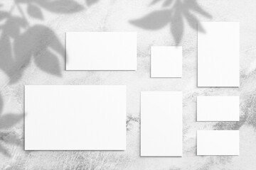 Composition of empty white different size watercolor sheets of paper and shadow from leaves on a light gray concrete background. Advertising board, mockup on the wall. Flat lay, top view, copy space