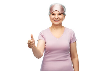 Fototapeta na wymiar old people concept - portrait of smiling senior woman in pajamas and eye sleeping mask showing thumbs up over white background