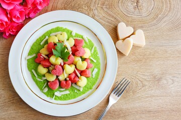 Heart shaped gnocchi with green peas cream sauce on top with grated parmesan cheeses on plate with pink roses bouquet and  heart shape parmesan on wooden table.Love concept for celebrate Mother's day