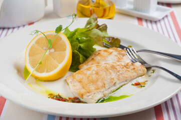 pike perch fillet fried with lemon on a white plate in a restaurant