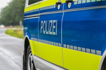 Side view of a German police car. Police lettering on the body from the passenger side. Blue background and yellow color with reflective stripes. Highway in the background © Marco