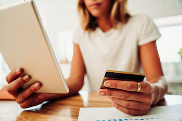 Caucasian student purchasing online holding credit card and digital tablet standing in kitchen