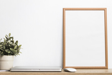 A white photo wooden frame with computer and plant on table.