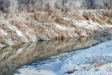 Trees and plants near the river are covered with frost on a cold winter sunny day