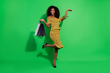 Full size portrait of carefree funky dark skin lady hold bags raise hand palm isolated on green color background
