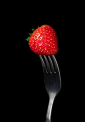 Strawberry berry close-up on a fork, on a black background