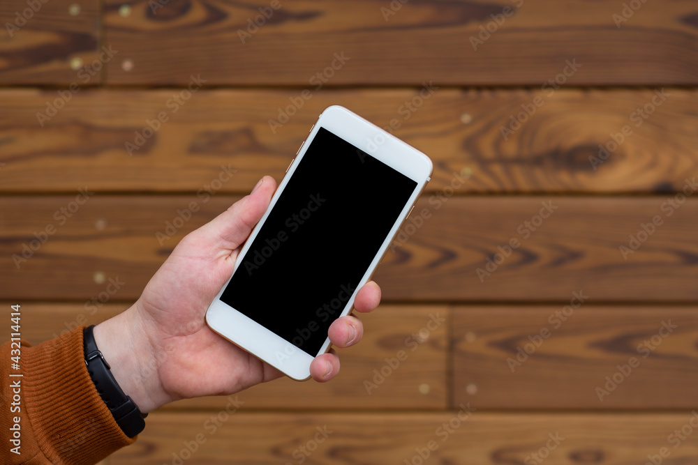 Aufkleber man holds a mockup of a smartphone with a black display close-up on a wooden background.