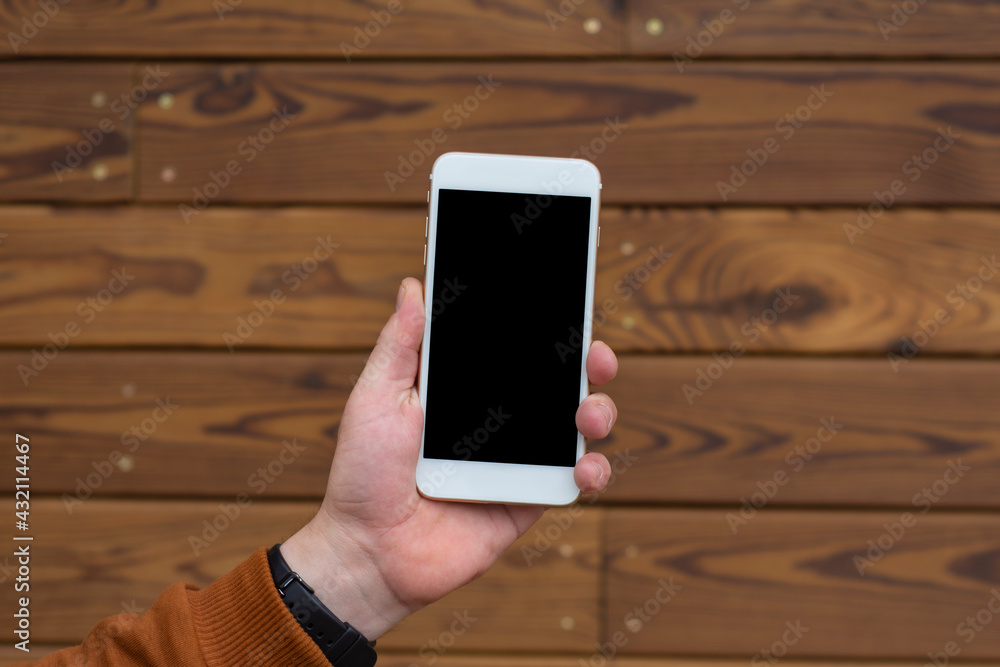 Poster man holds a mockup of a smartphone with a black display close-up on a wooden background.