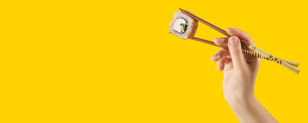 Women's hands hold sushi rolls with sticks. Yellow background. Creative concept