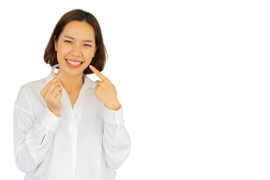 close up young asian woman smiling with hand holding dental aligner retainer (invisible) isolated on white background of dental clinic for beautiful teeth treatment course concept