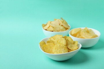 Bowls with potato chips on mint background