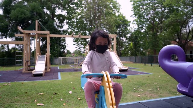 Little girl with protective face mask playing at playground.