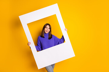 Portrait of attractive cheerful girl holding in hands big paper frame photo shop isolated over bright yellow color background
