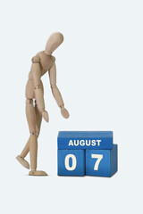 day of the month 07 August calendar . A calendar date on blue cubes and a wooden man standing next to it. White background