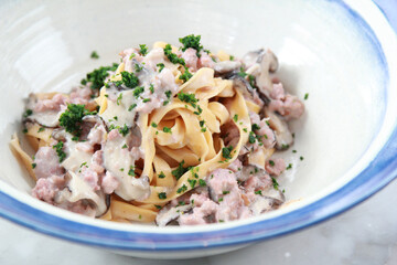 Pasta fettuccine with mushrooms and fried chicken ham in creamy cheese sauce on a light wooden background