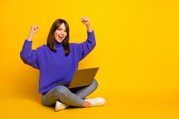 Portrait of attractive cheerful lucky girl sitting in lotus pose using laptop rejoicing isolated on bright yellow color background