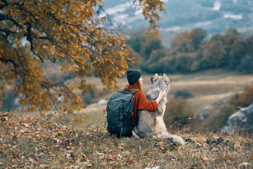 woman hiker with a backpack next to a dog admires the nature of the mountain