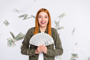 Portrait of attractive cheerful red haired girl holding cash salary freelance flying waste isolated over white light color background