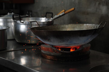 Chef cooking with a wok in fire on charcoal in a kitchen (Asian food, Thai Chinese culinary)