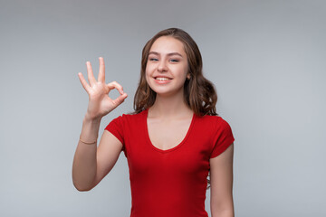 Fototapeta premium Excellent job. Attractive young brunette woman in red t shirt showing OK sign and smiling, give positive reply