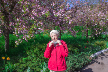 Positive smiling senior woman takes off protective medical mask from face outdoors. Concept of happy end. Pollen allergy. Victory over coronavirus. Pandemic Covid-19. Green trees at spring.