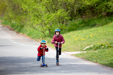 Obraz premium Children, brothers, riding scooters in the park together