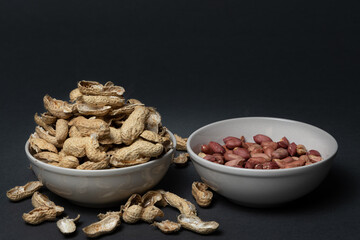 One bowl with peeled peanuts and another one full of peanut shells