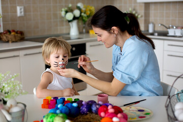 Mother painting on little blond toddler boys' face easter bunny