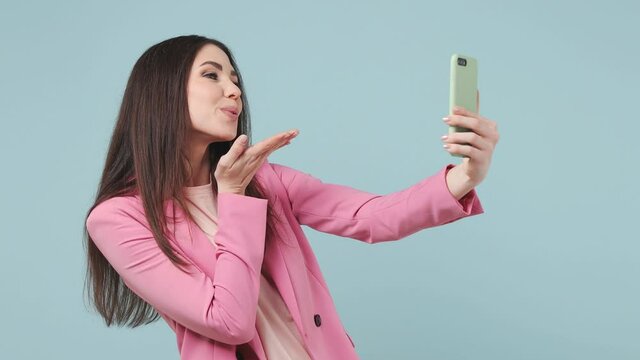 Beautiful fun brunette long hair young woman 20s years old wears pink jacket t-shirt doing selfie shot on mobile phone post photo on social network isolated on pastel blue wall color background studio