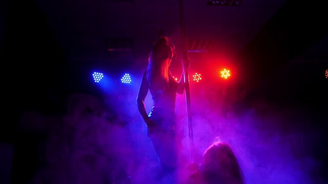 A flexible dancer dances on a pole under the light of colorful spotlights.