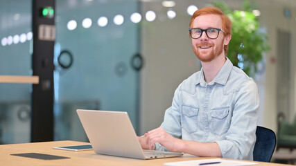 Cheerful Businessman with Laptop Smiling at Camera in Office 