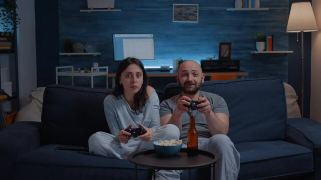 Determinated excited couple winning video games, hugged each other sitting on sofa playing, happiness scream enjoying online competition. Competitive gamers using joysticks playstation gaming