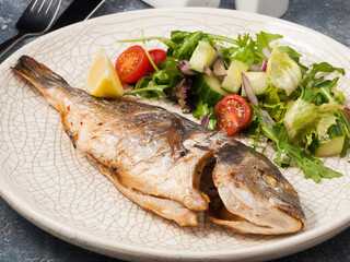 Dorado on coals with fresh vegetables on a light plate