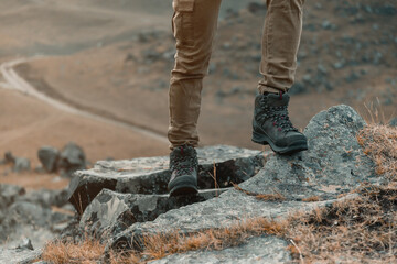 Hiker woman standing on rocky stone on background of mountain river, view of boots.