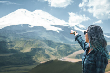 Young woman traveler pointing at snowy high mountain.
