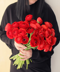 Young woman with a gift bouquet of red ranunculus, mono bouquet of passion in woman hands. 